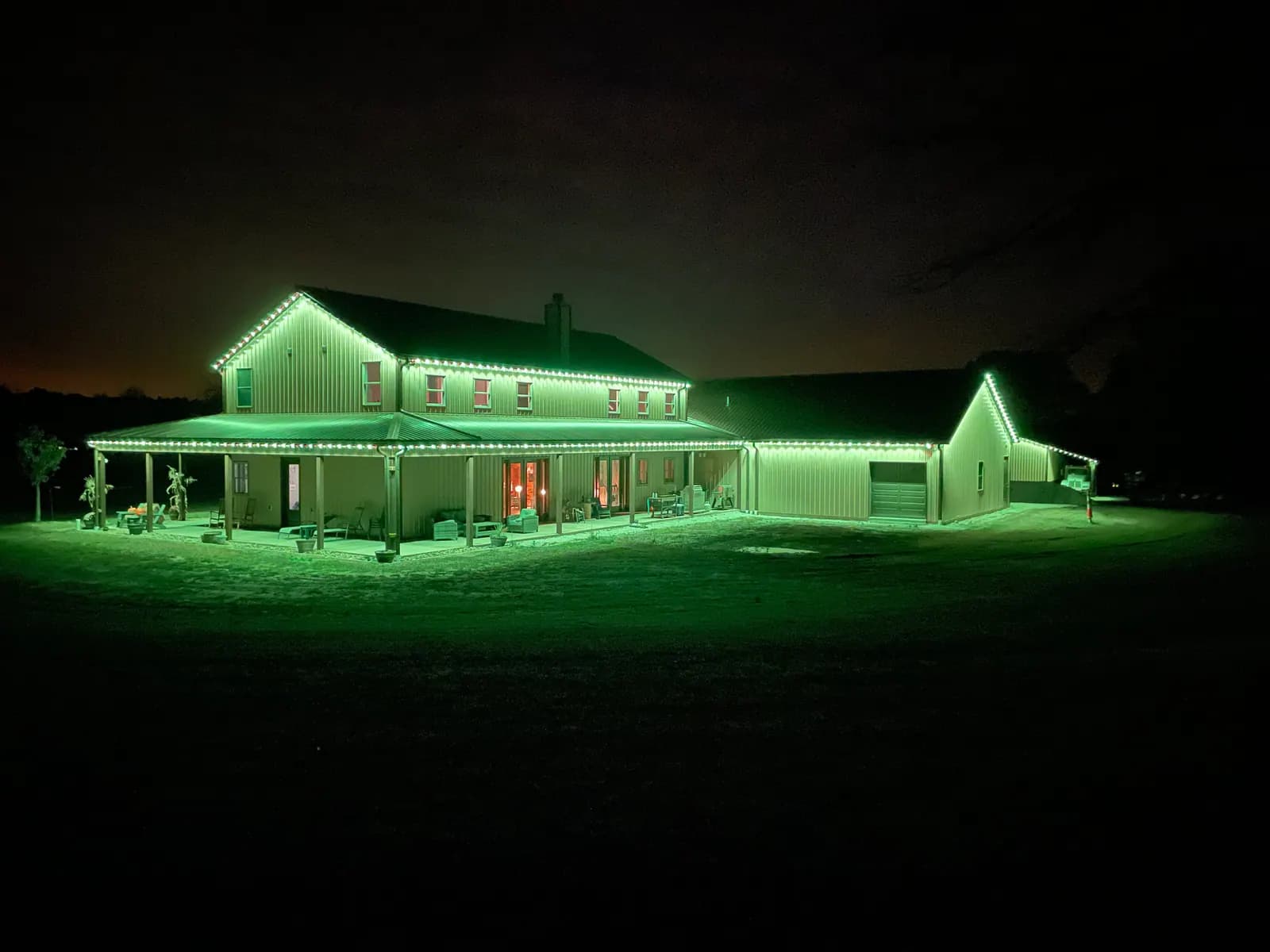 Country home and attached shop with every roofline outlined in green permanent LED lights at night