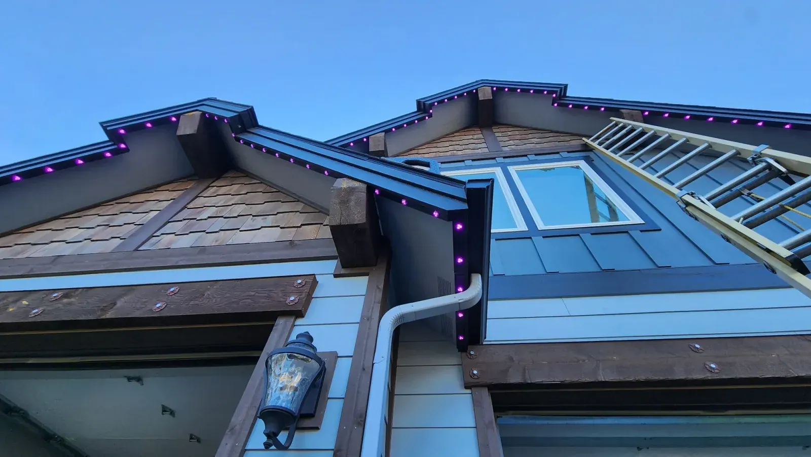 Craftsman-style cedar shake home with purple permanent LED lights along the rooflines at night