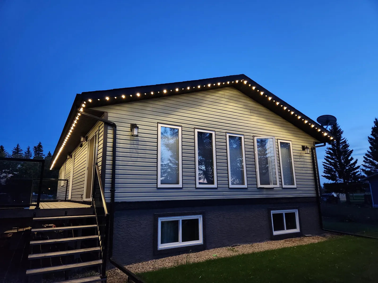 The same bungalow at twilight with a soft warm white glow from permanent LED soffit lights - everyday architectural lighting
