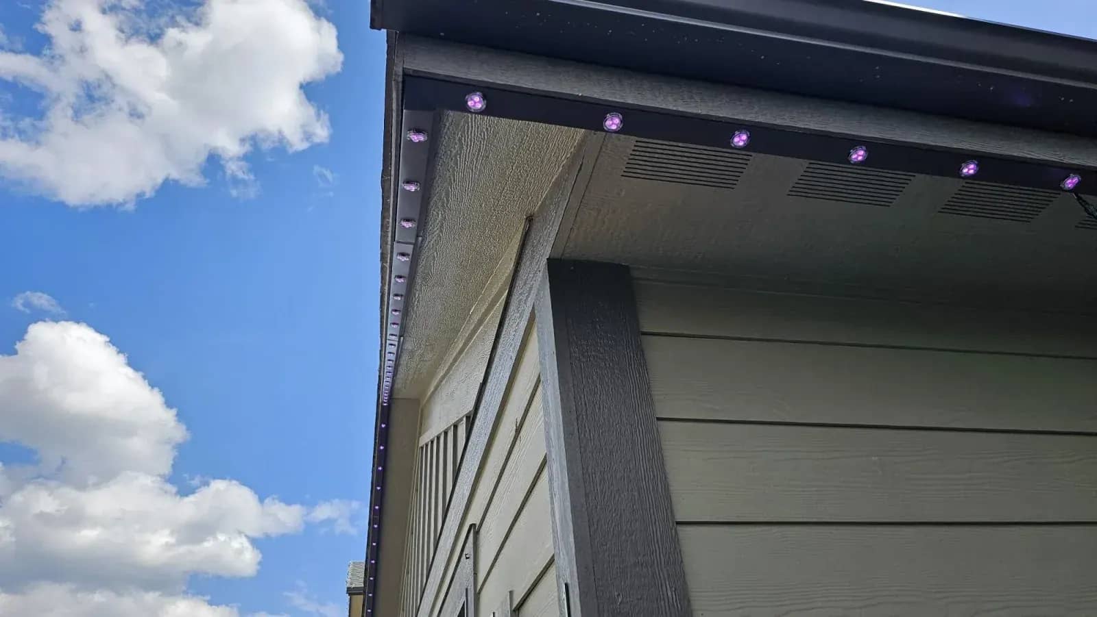 Close-up of a black aluminum permanent LED track with purple RGB light pucks mounted under an eave